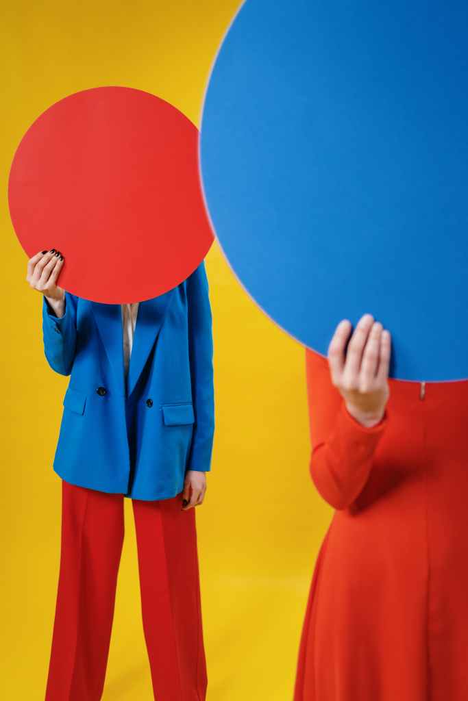 Anonymous trendy ladies covering faces with colorful sheets in studio
